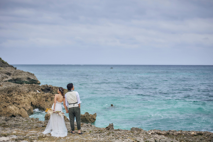 沖縄の海岸で手をつなぎ佇む新郎新婦